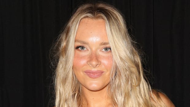Camille Kostek sports her blonde hair in a soft wave and smiles for the camera.